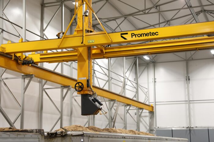 Automated bridge crane sampler operating inside a biomass fuel receiving facility to collect representative fuel samples.