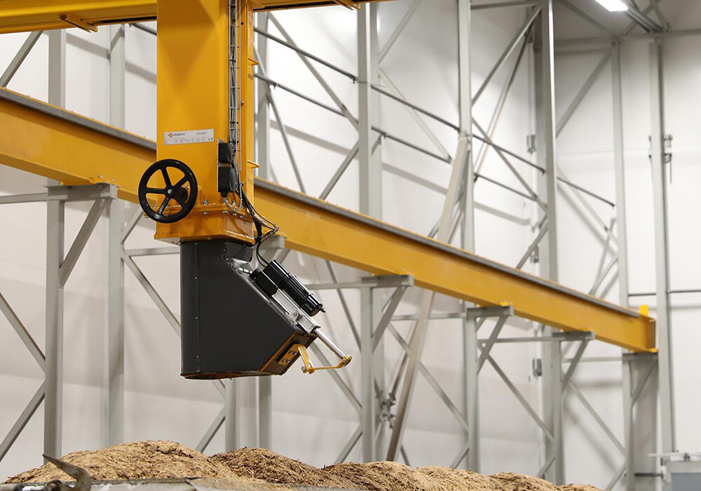 Bridge crane sampling system positioned above biomass fuel load for automated representative sample collection.